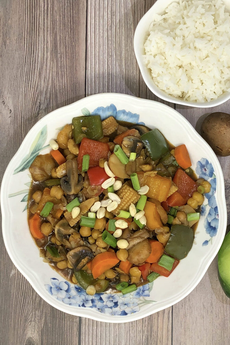 chickpea vegetable kung pao in a bowl served with rice, half green pepper and mushroom in background