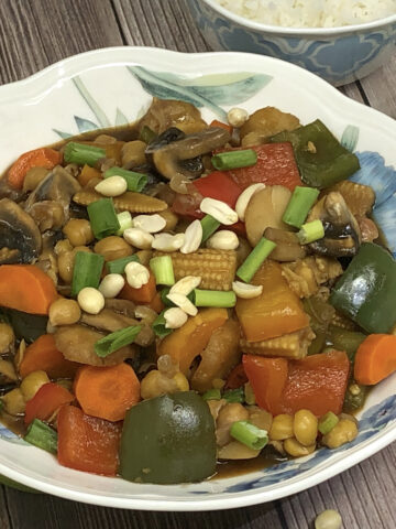 chickpea vegetable kung pao in a bowl served with rice, half green pepper and mushroom in background
