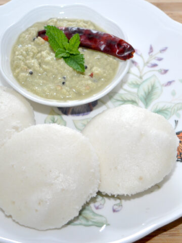 idli in a plate with sambar in background
