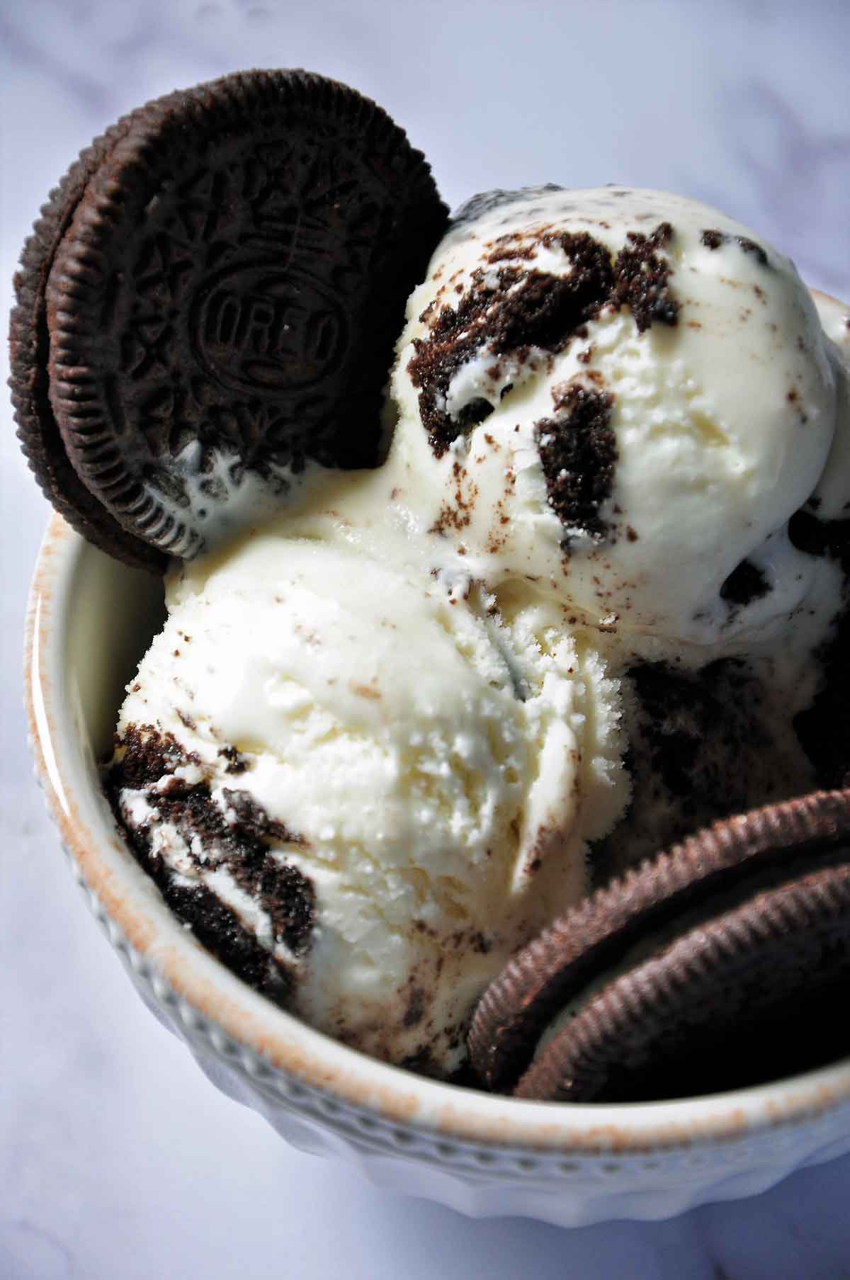 Two scoops of Oreo ice cream with 2 oreo cookies in a bowl.