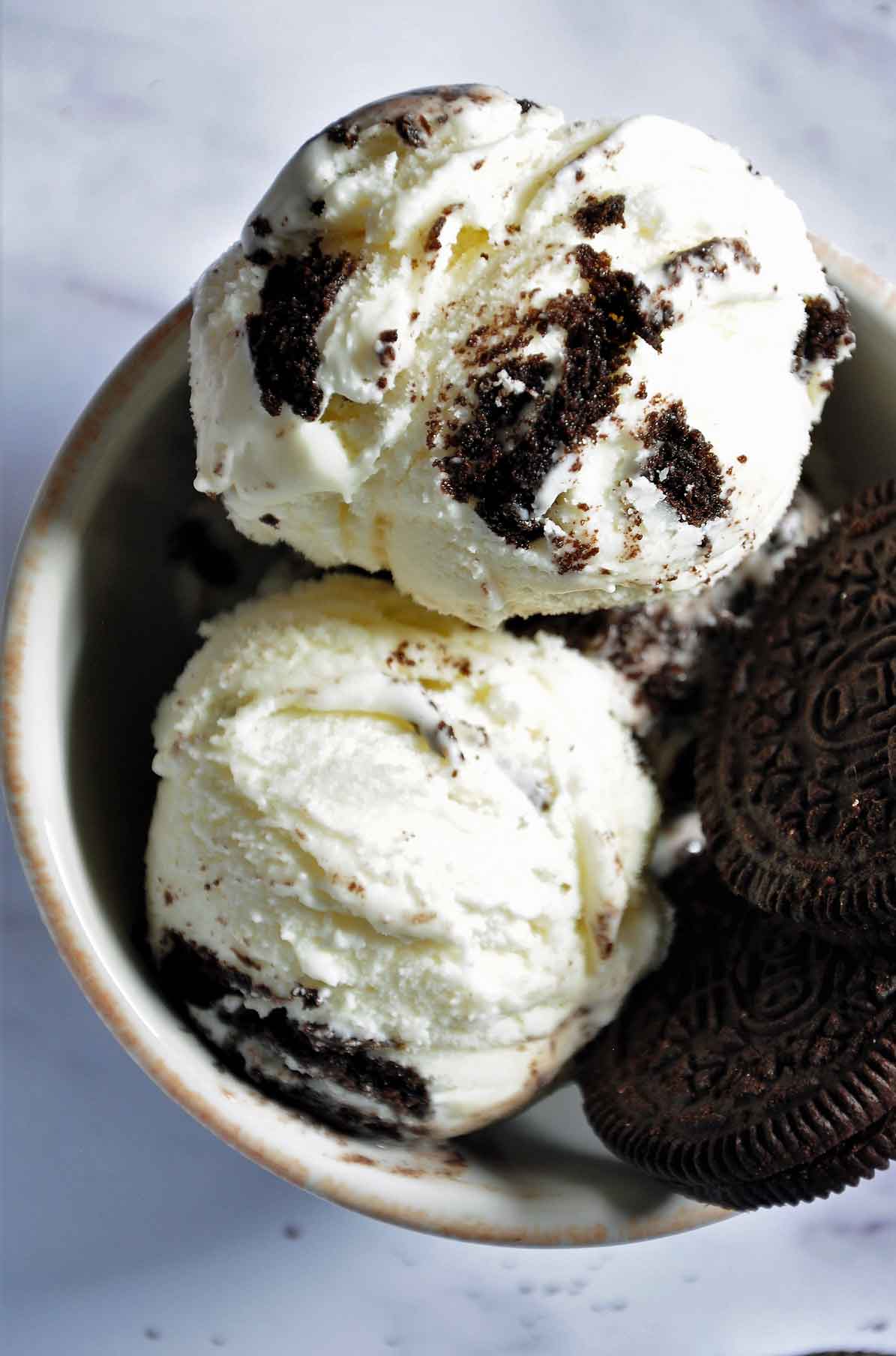Two scoops of Oreo ice cream with 2 oreo cookies in a bowl.