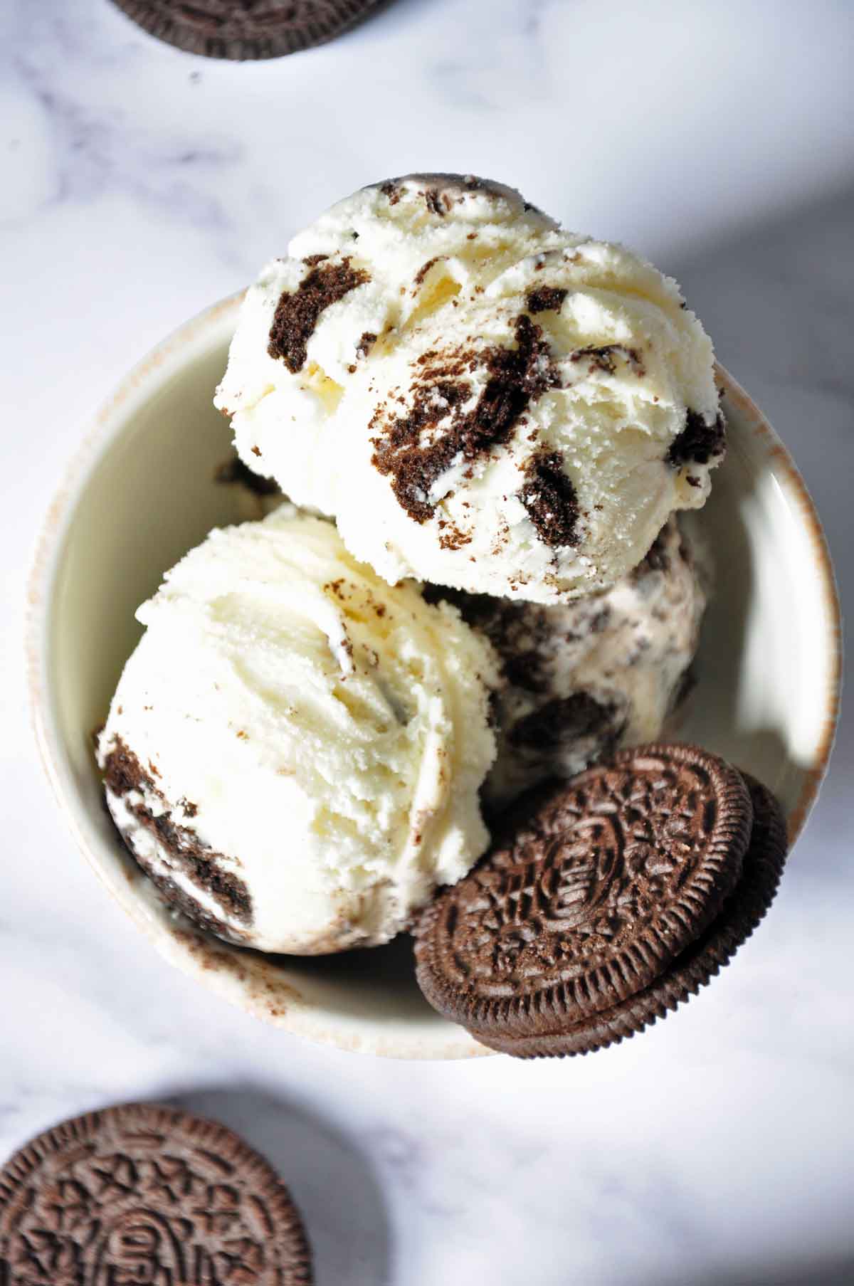 Three scoops of Oreo ice cream with 1 oreo cookie in a bowl and 1 oreo cookie in the foreground.