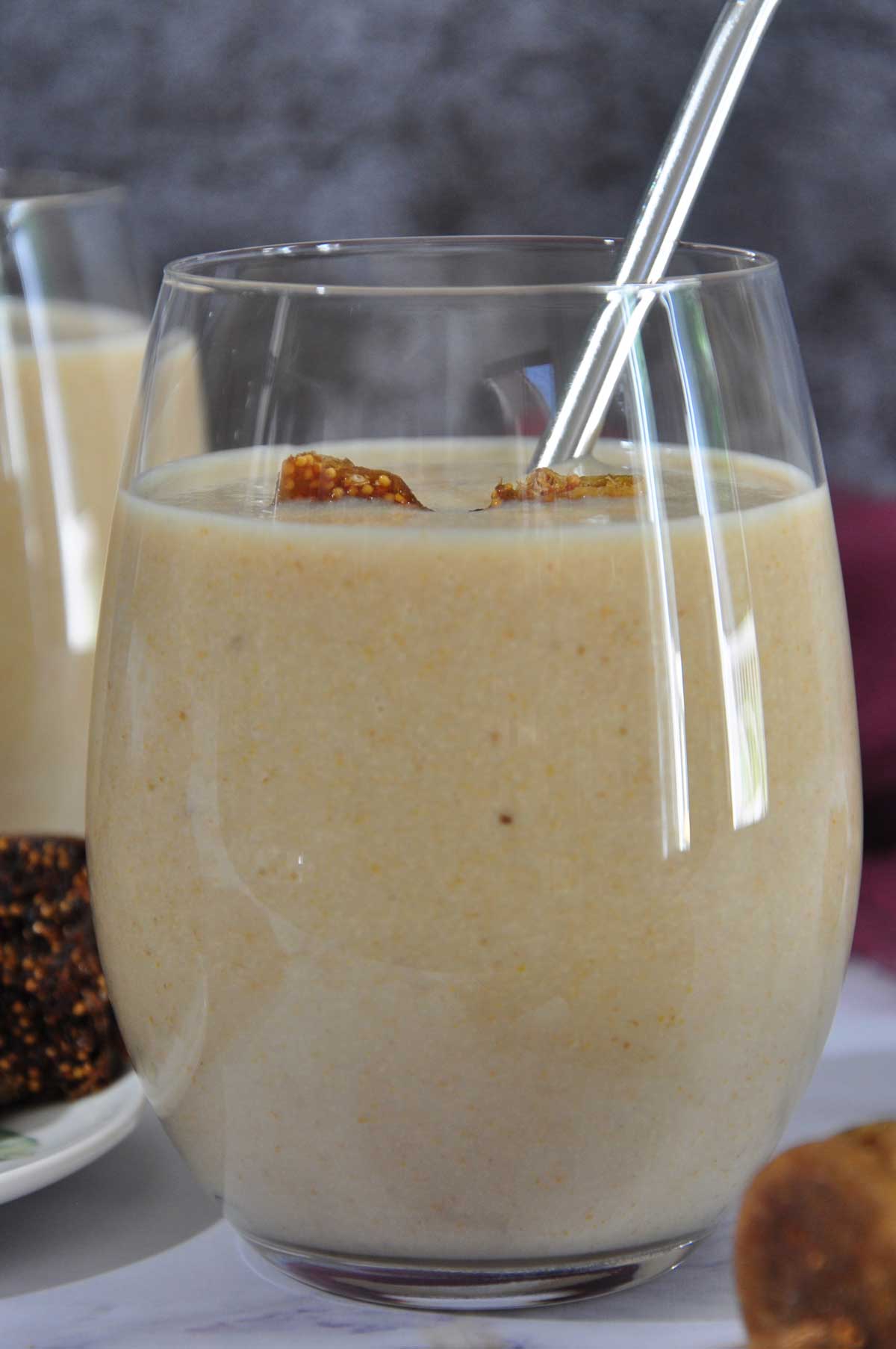 Fig smoothie in a glass with a steel straw and figs in the background.