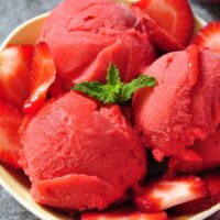 closeup of strawberry sorbet scoops with sliced strawberries in a fruit bowl.