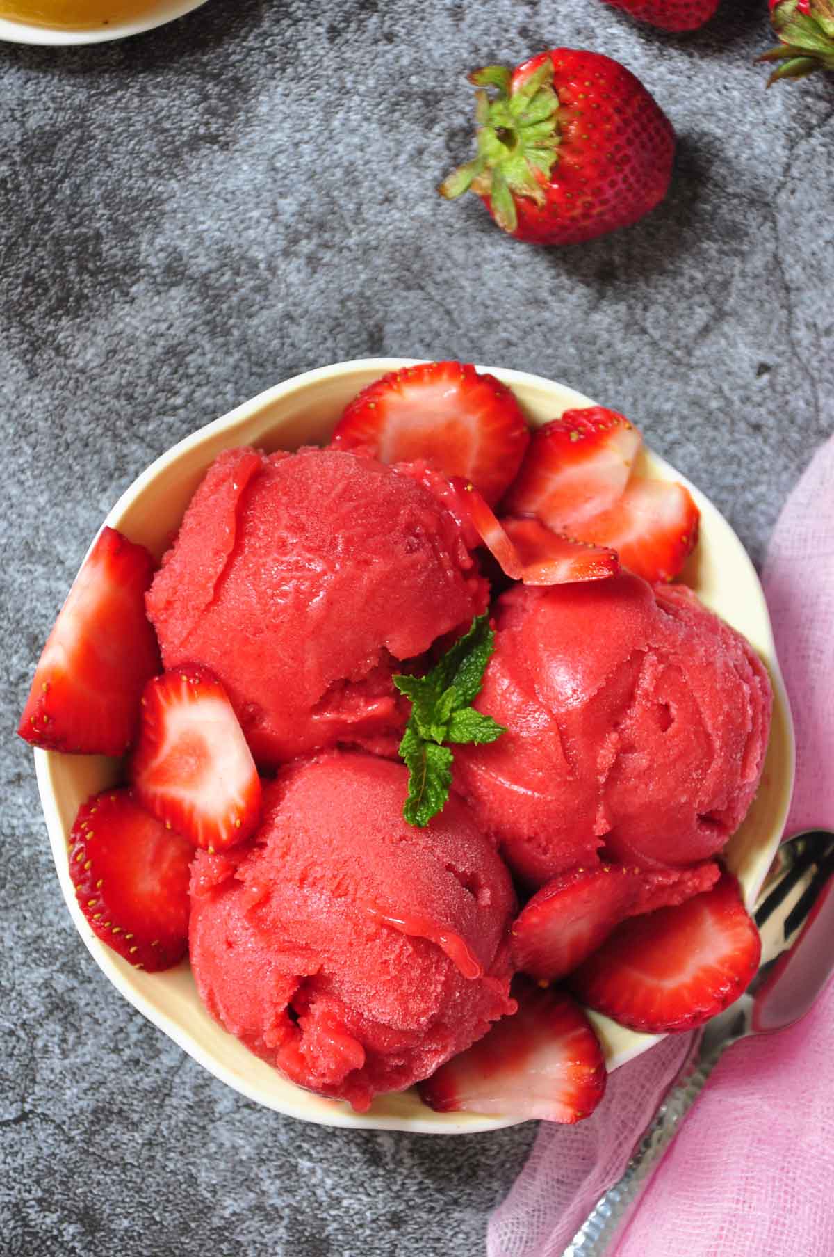 strawberry sorbet scoops with sliced strawberries in a fruit bowl.