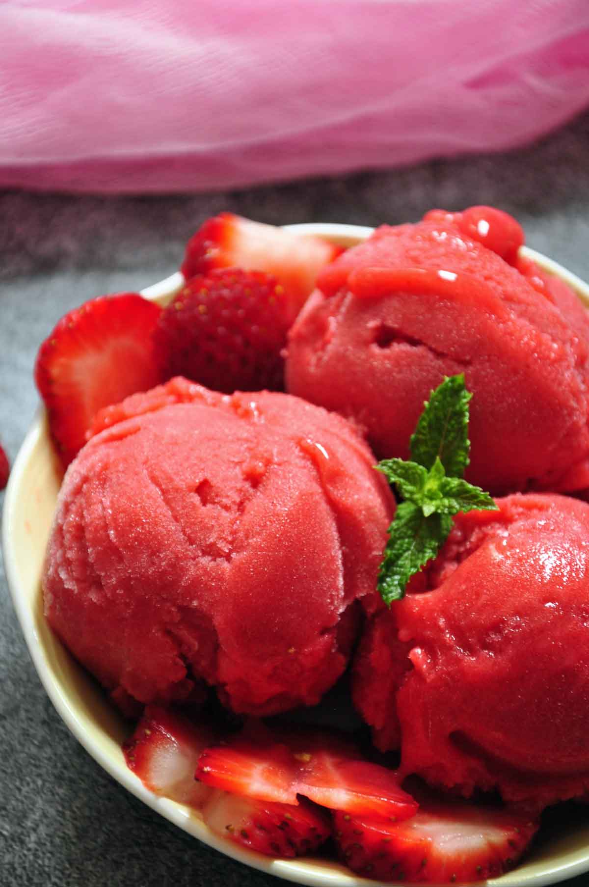 strawberry sorbet scoops with sliced strawberries and mint leaves in a fruit bowl.
