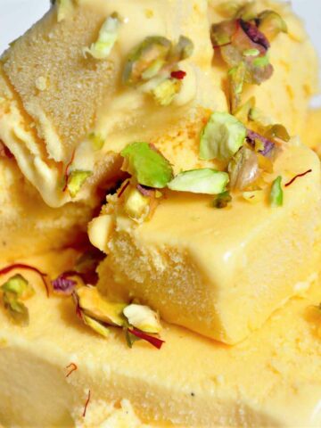 Cubes of mango kulfi in a plate and garnished with pistachio.
