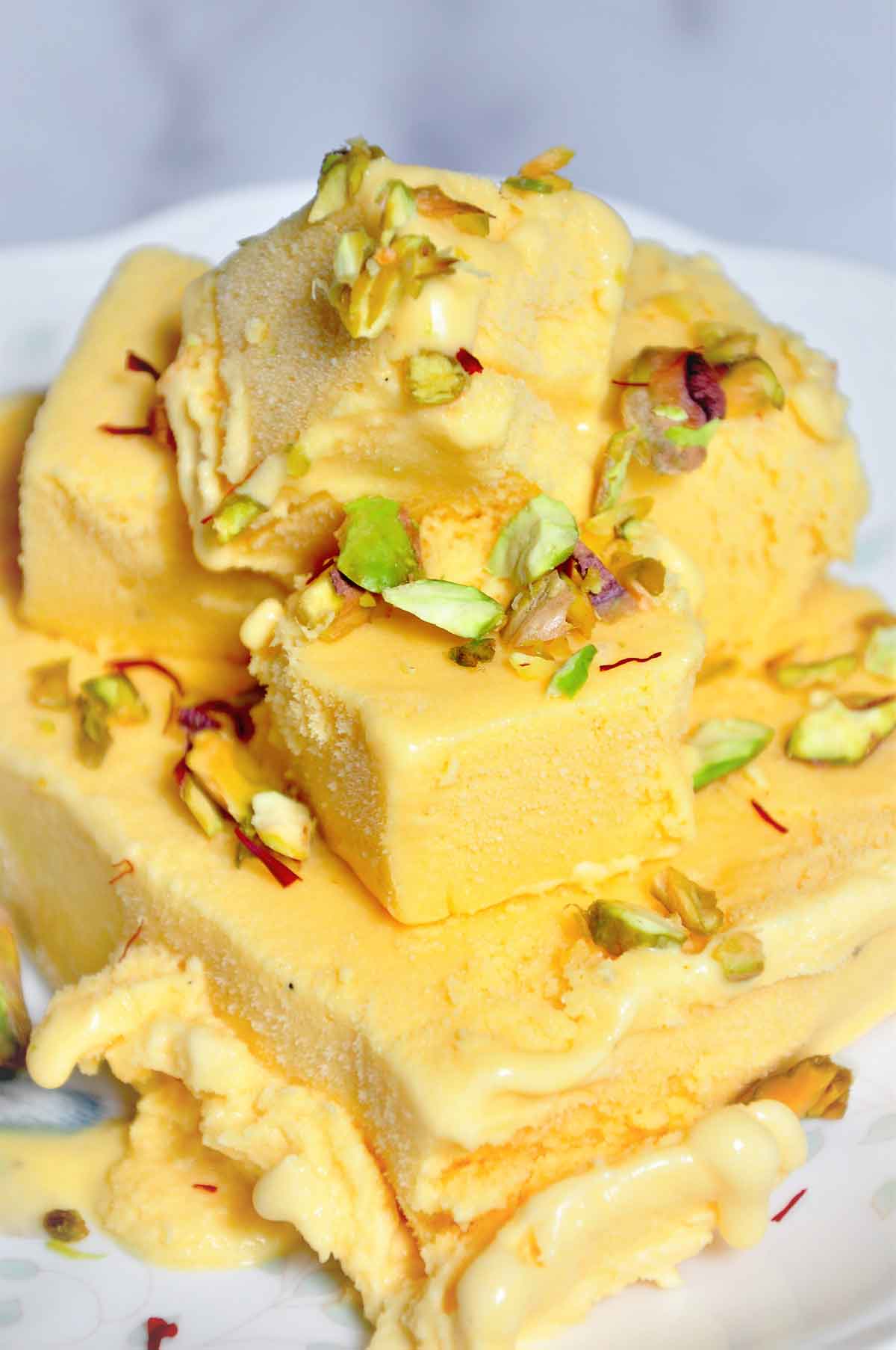 Cubes of mango kulfi in a plate and garnished with pistachio.