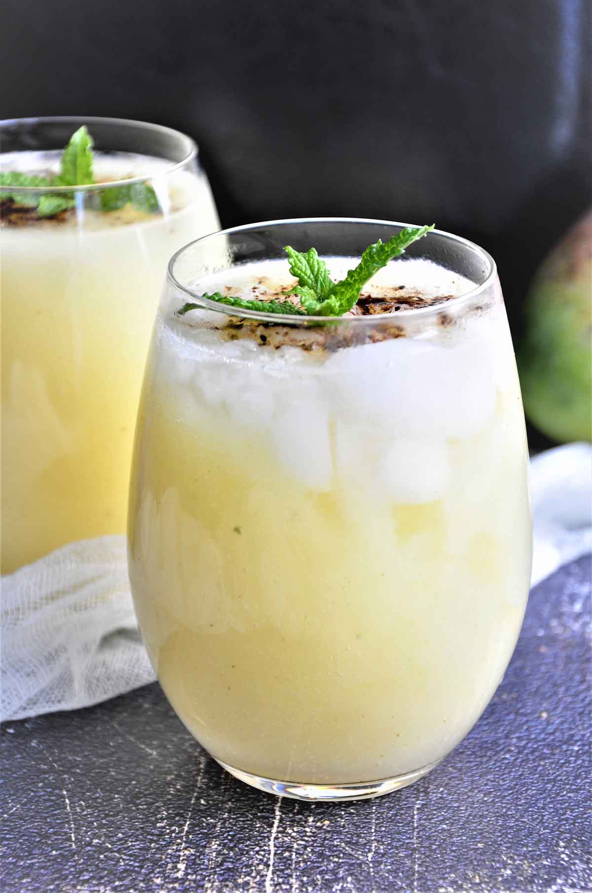 Raw mango sweet and sour drink in a glass garnished with mint leaves.