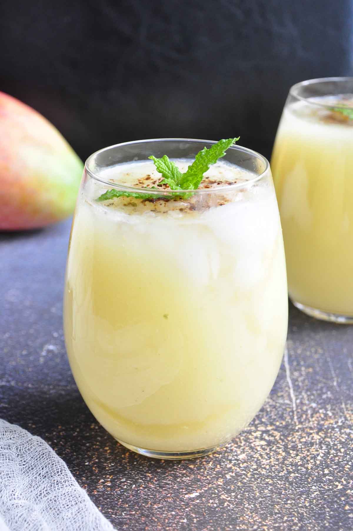 Raw mango sweet and sour drink in a glass garnished with mint leaves.