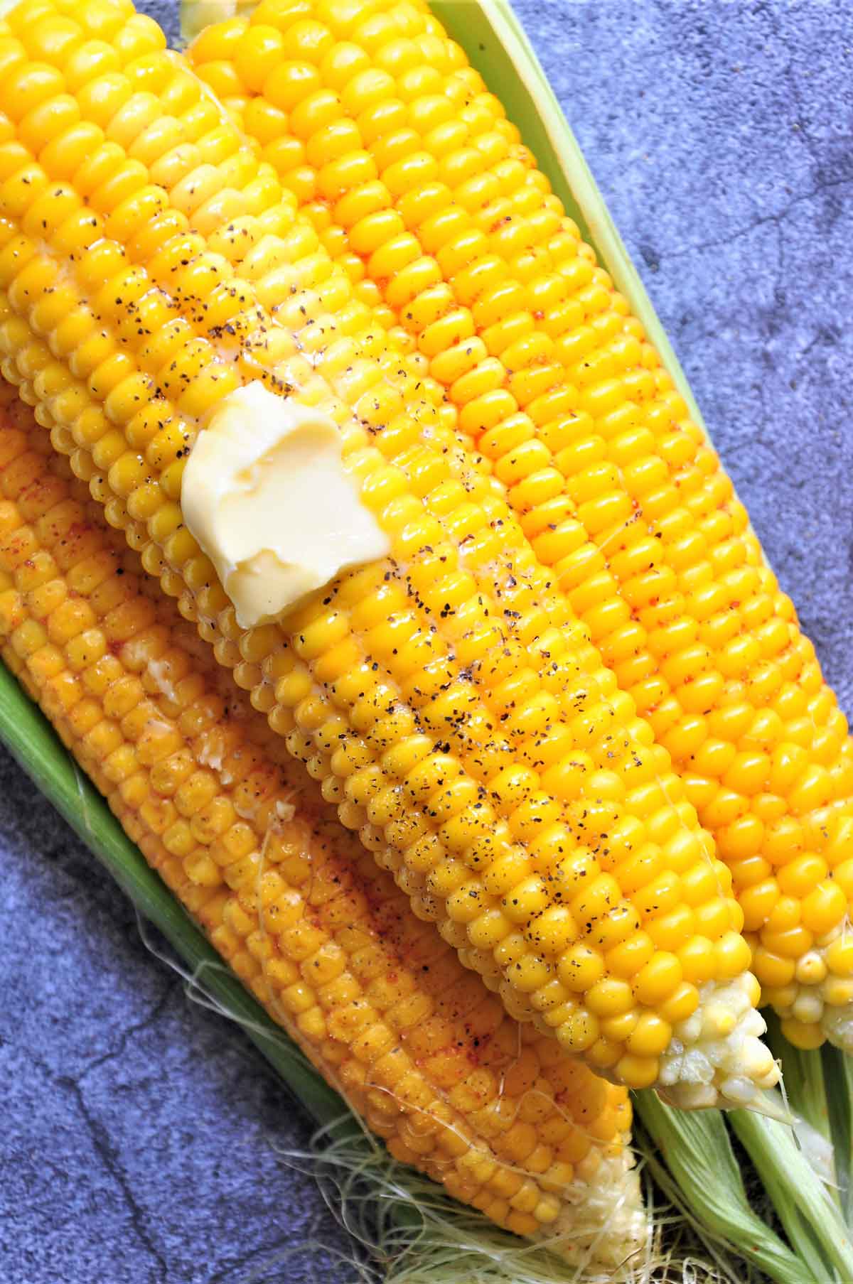 Three corn on the cob with seasoning.