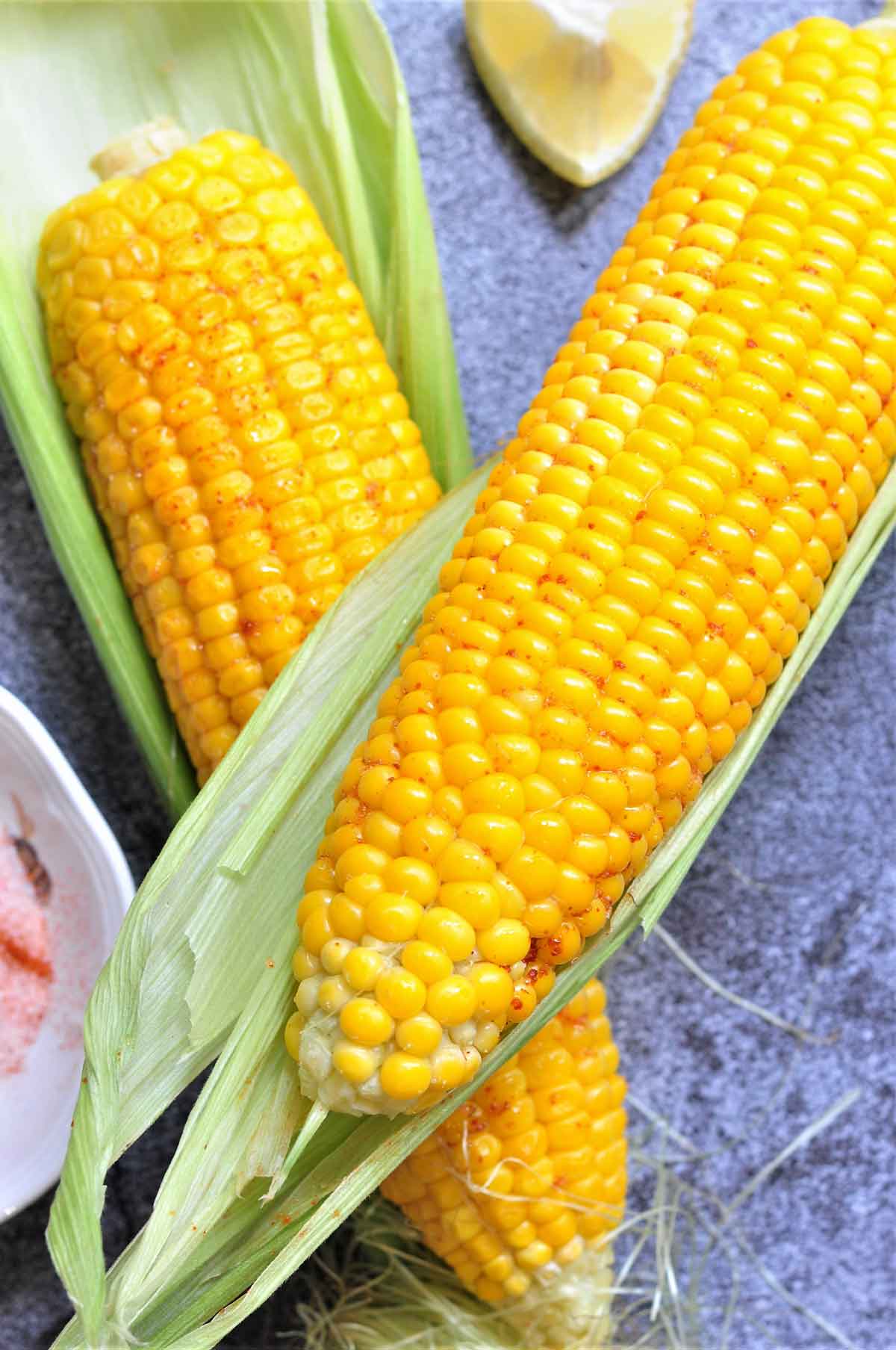 Two corn on the cob with seasoning.