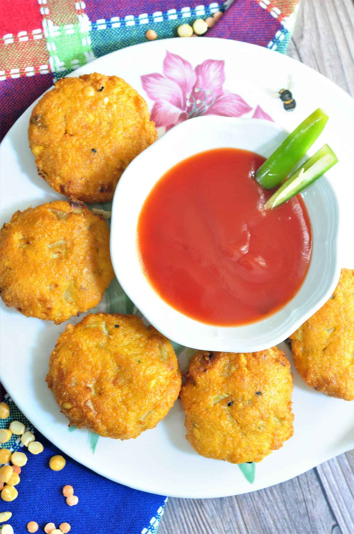 Five lentil fritters served in a plate with ketchup on the side.