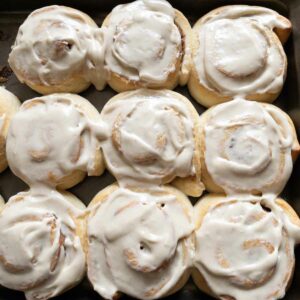 9 cinnamon rolls in a baking tray with icing on top.