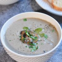 Cream of mushroom soup in a bowl garnished with cooked sliced mushroom and cilantro.
