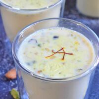 Sweet Almond milk in a glass, garnished with chopped nuts and saffron strands.