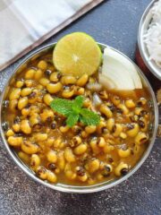 Black eyed pea curry served in a metallic bowl and garnished with sliced lime and onion.