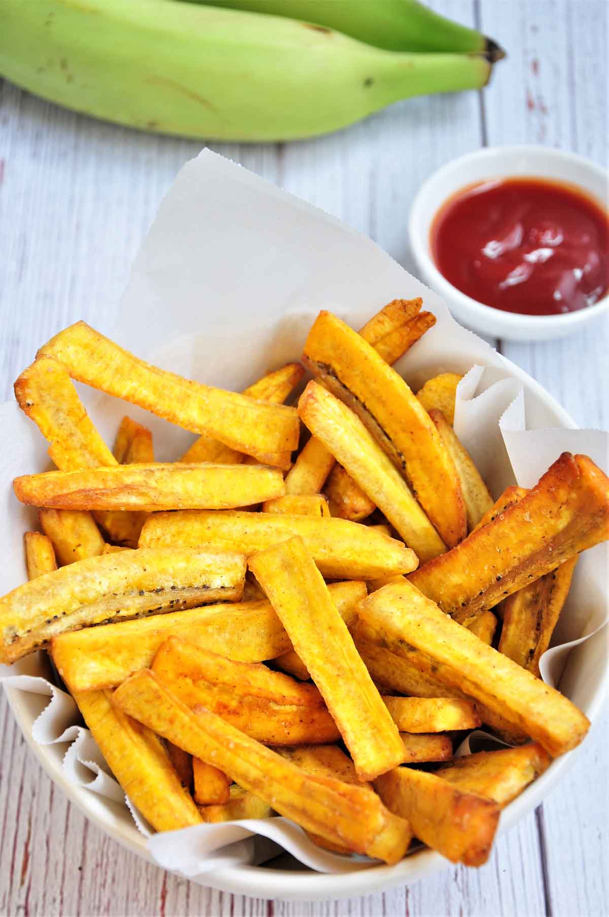 Plantain fries served in a bowl with ketchup on the side.