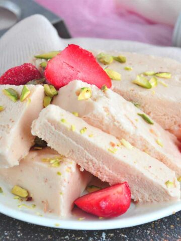 Strawberry kulfi chunks served in a plate with cut strawberry.