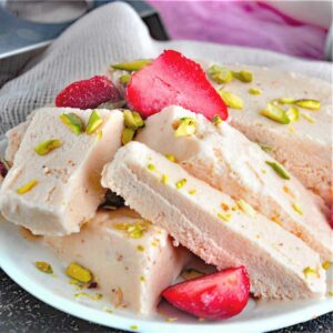 Strawberry kulfi chunks served in a plate with cut strawberry.