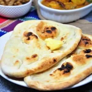 Two naans served in a plate with a dollop of butter.