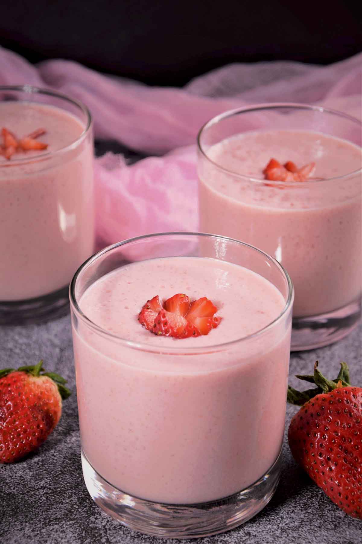 Strawberry milkshake served in a glass and topped with strawberry.