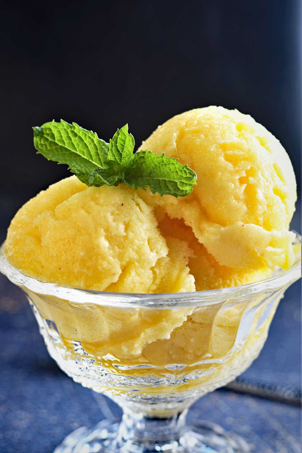 Pineapple sorbet ice cream scoops in a glass stem bowl with mint leaves.