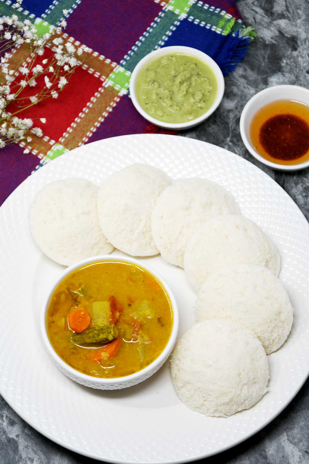 Idlis served in a plate with a bowl of sambhar and chutney.