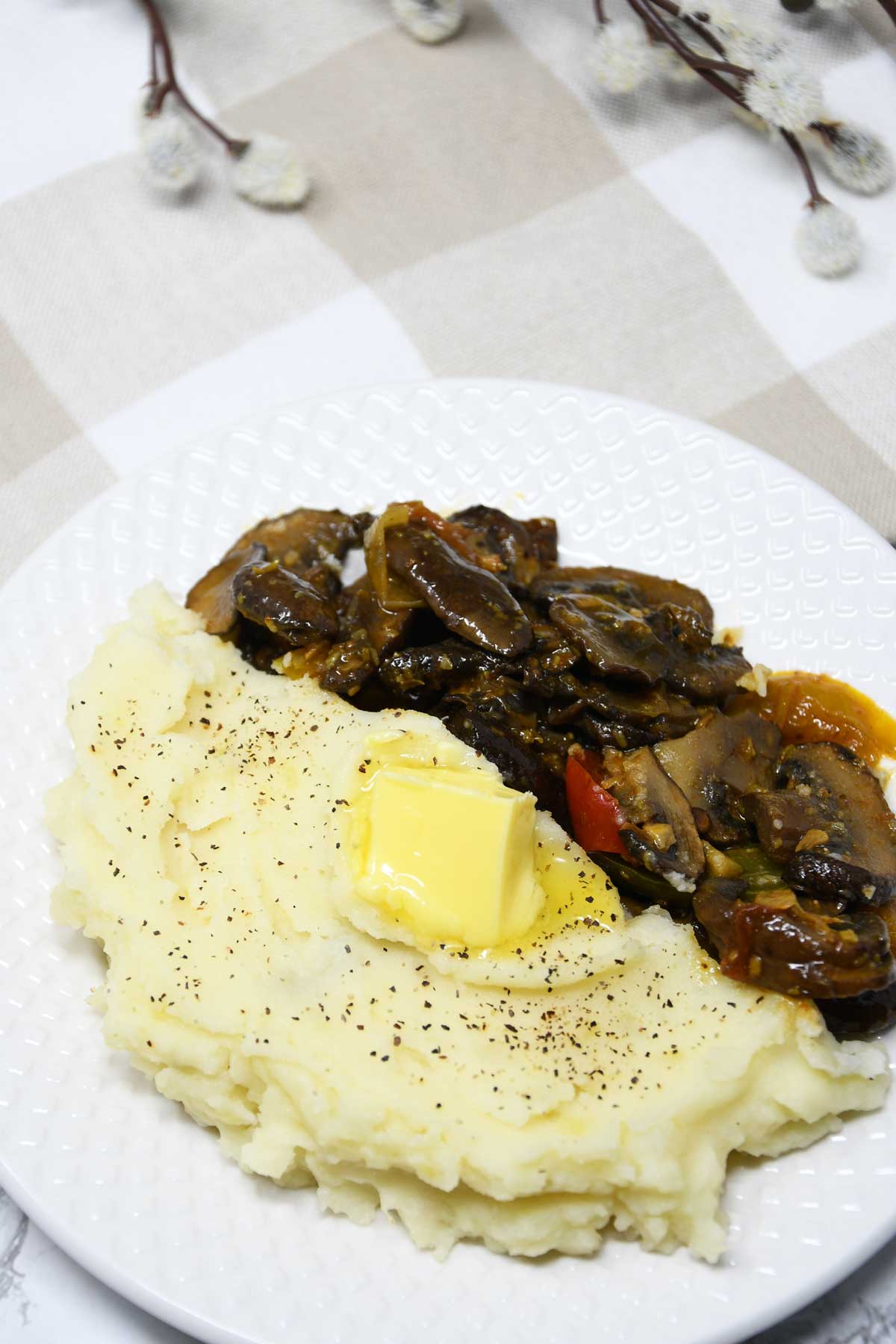 Mashed potato in a plate with butter cube as topping and mushroom sides.