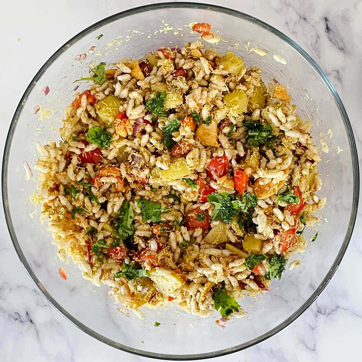 Bhel mix in a glass mixing bowl.
