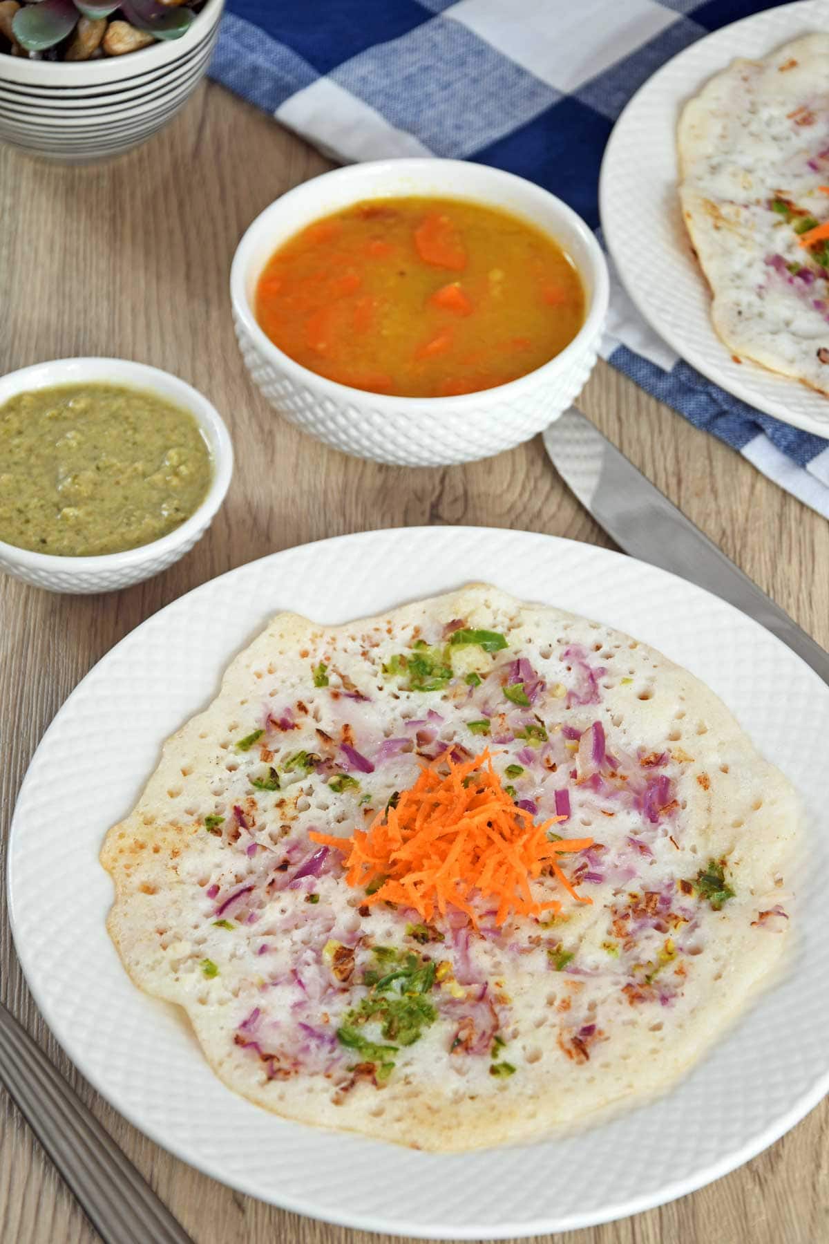 Uthappam served on plate with sambhar and chutney.