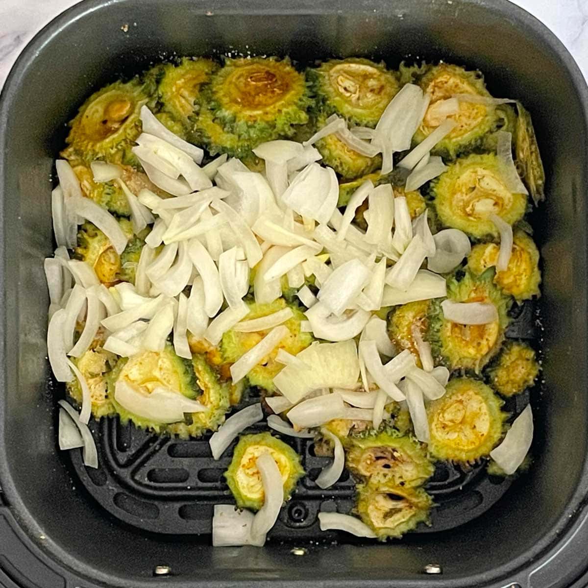 Bitter gourd mixed with onions in Air fryer basket.