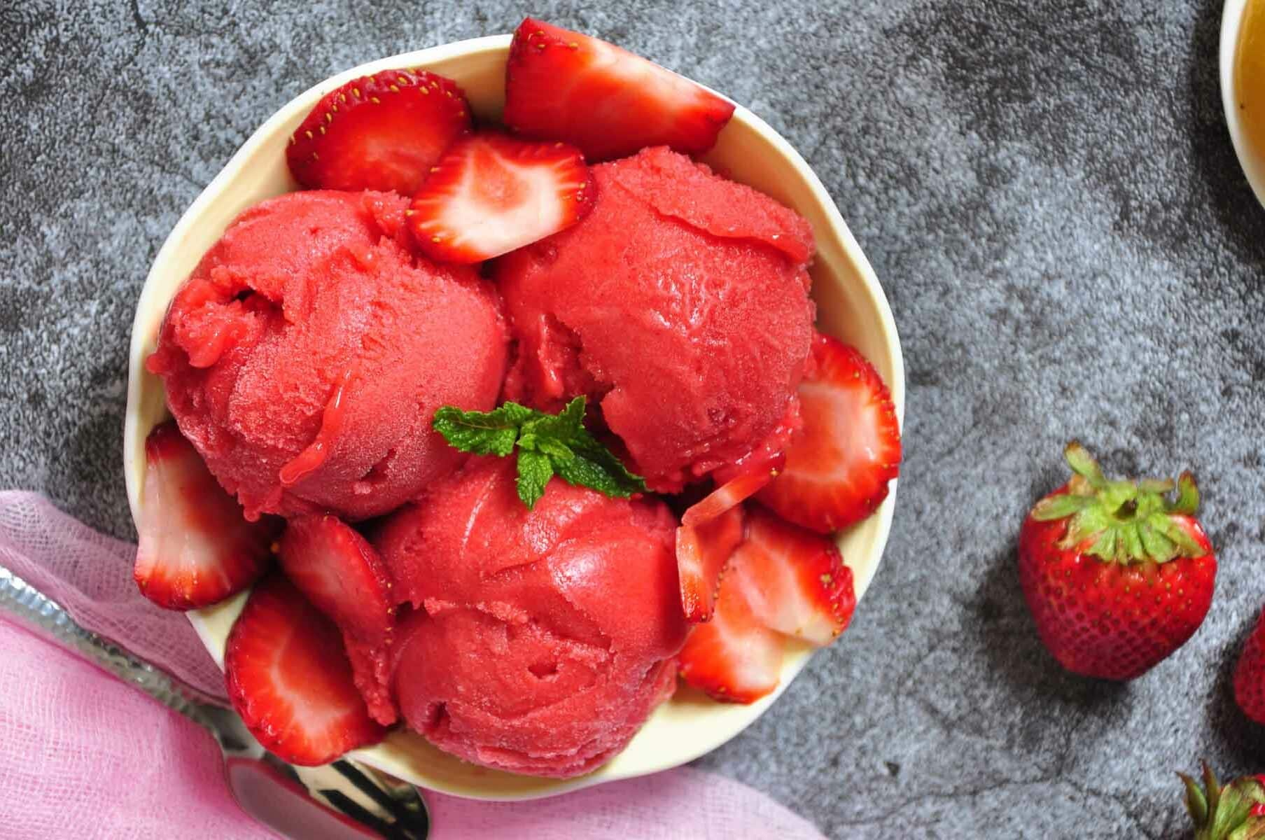 strawberry sorbet scoops with sliced strawberries in a fruit bowl.