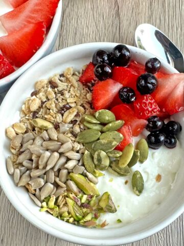 Creamy Greek yogurt fruit bowl with strawberries, blueberries, and mixed seeds. Perfect healthy snack or breakfast option.